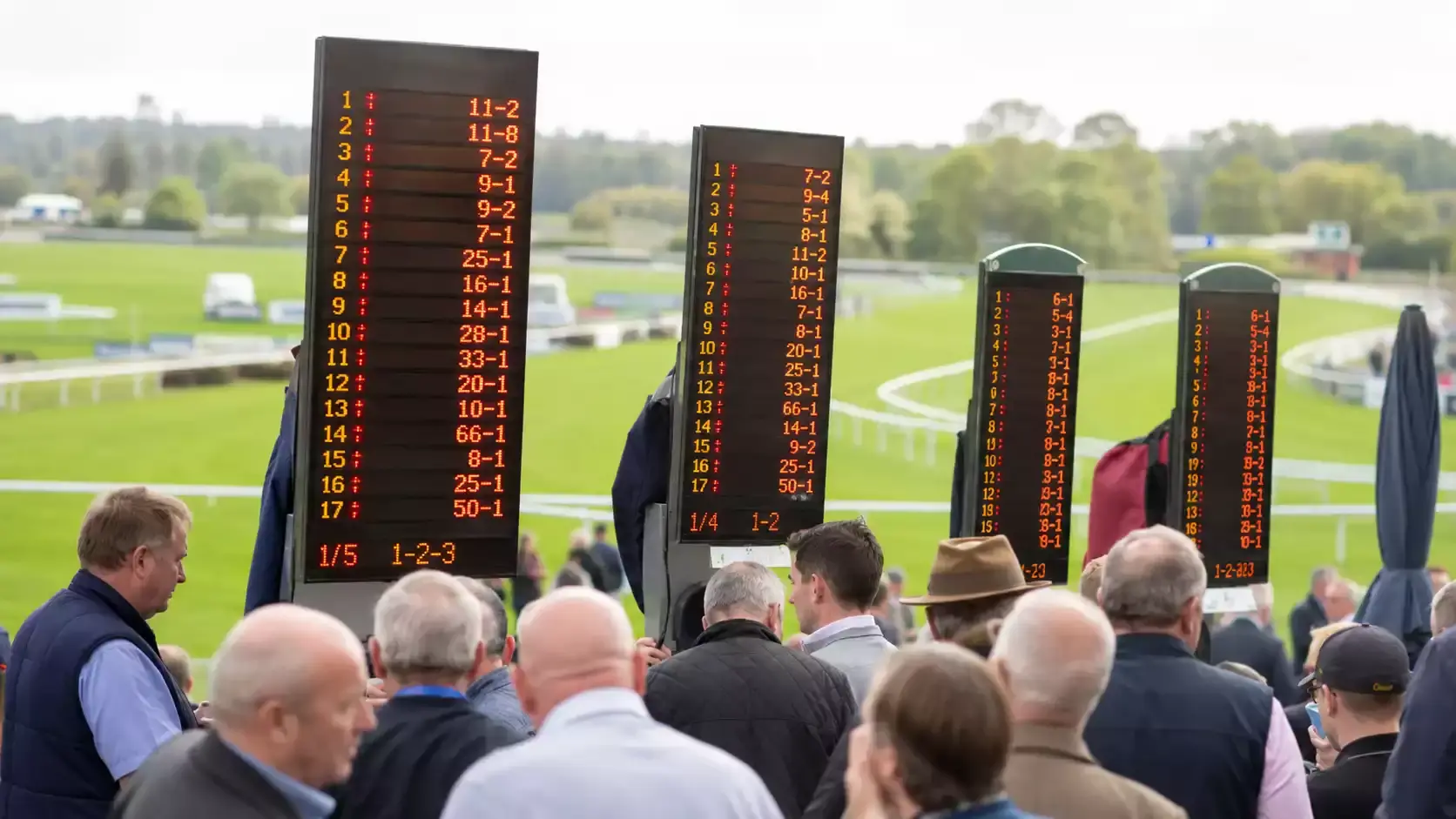 UK racecourse with bookmaker boards showing fluctuating odds before a horse race