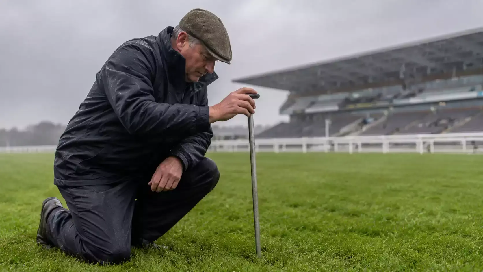 A clerk of the course inspecting the turf at a UK racecourse on a rainy morning before racing